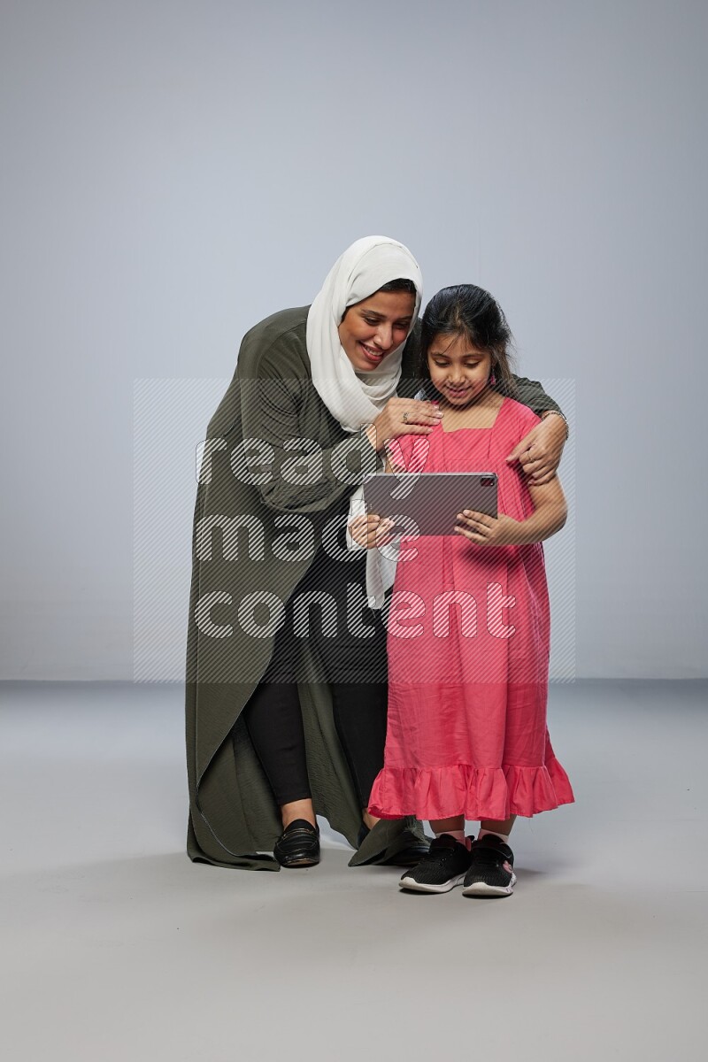 A girl holding an Ipad with her mother on gray background