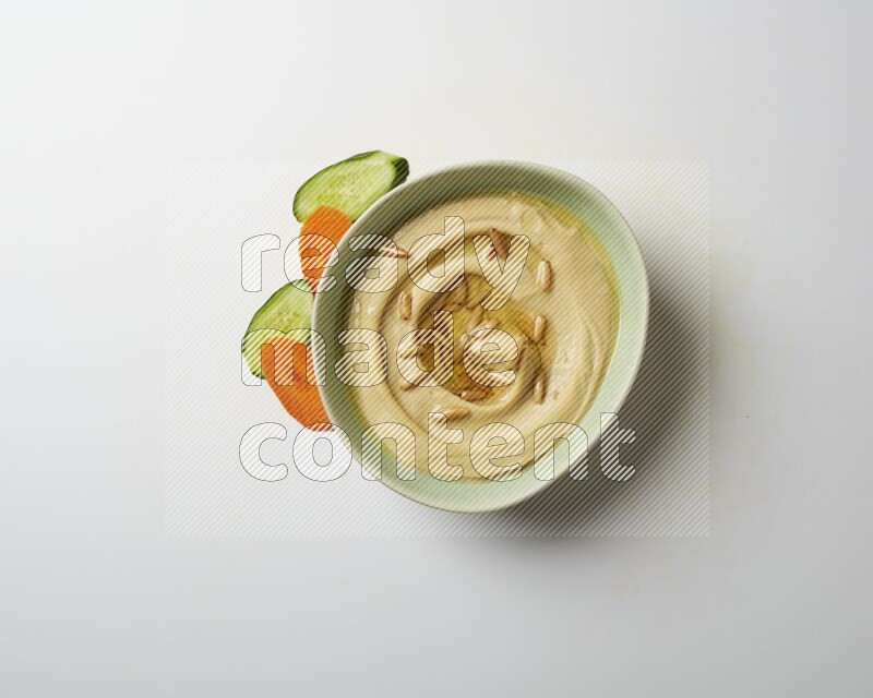 Hummus in a green plate garnished with pine nuts on a white background