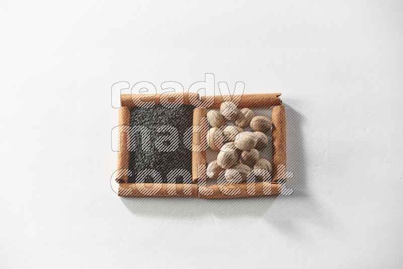 مربعان من أعواد القرفة ممتلئان بحبة البركة السوداء وجوزة الطيب علي خلفية بيضاء