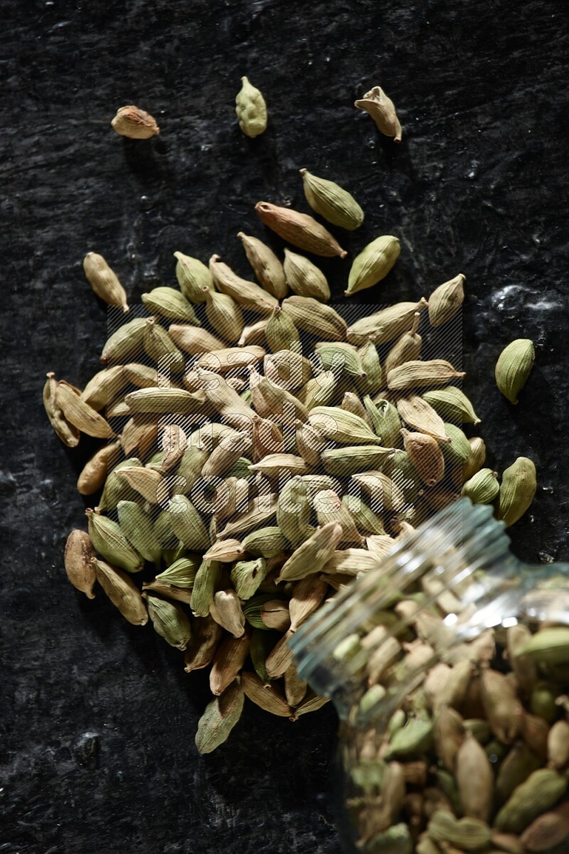 وعاء زجاجي للتوابل مقلوب ممتلئ بحبوب الهيل على خلفية سوداء