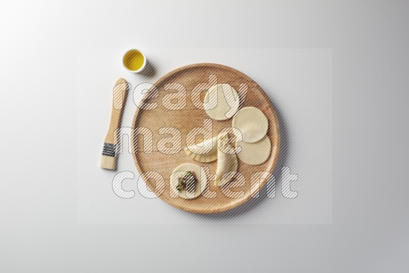 two closed sambosas and one open sambosa filled with meat while oil with oil brush aside in a wooden dish on a white background