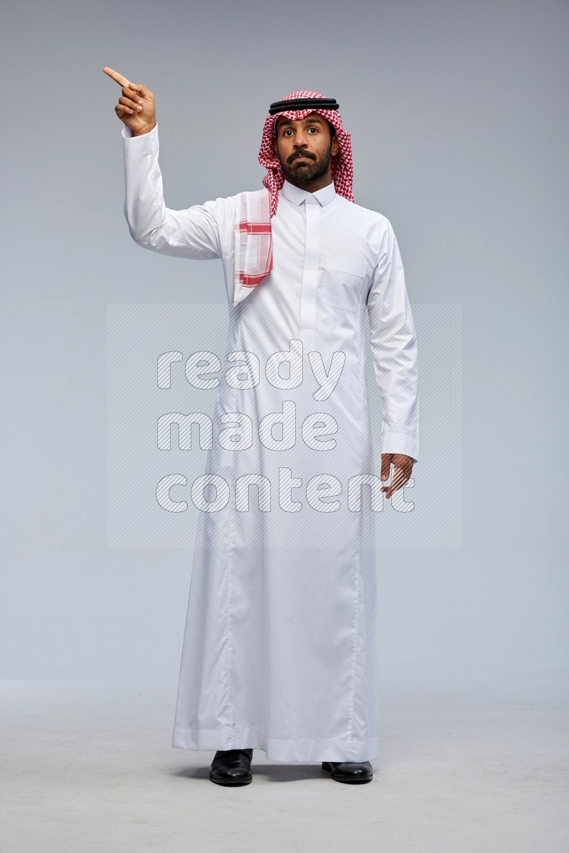 Saudi man Wearing Thob and shomag standing interacting with the camera on Gray background