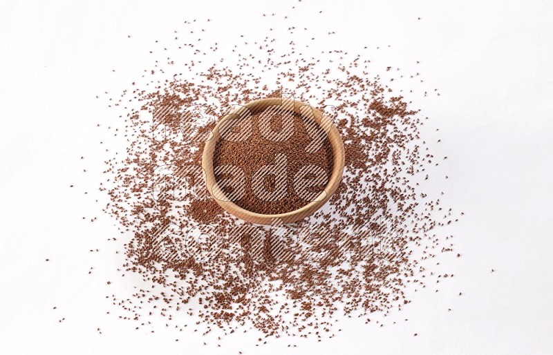 A wooden bowl full of garden cress seeds with more seeds spread on a white flooring
