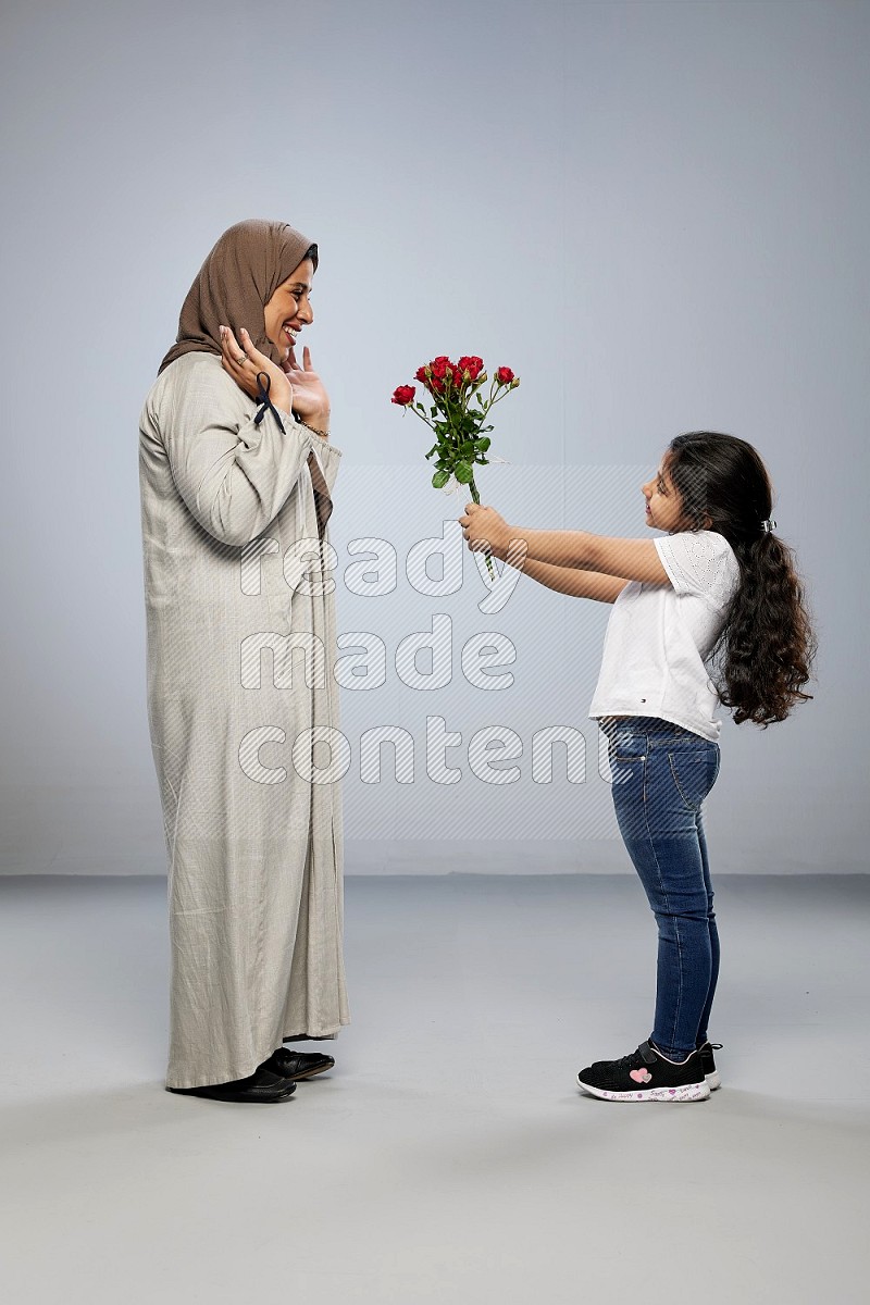 A girl standing giving flowers to her mother on gray background