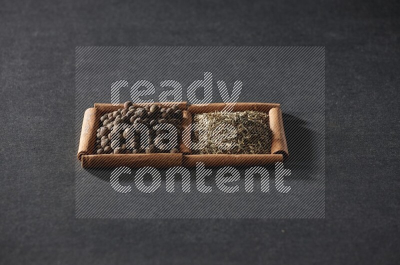 مربعان من أعواد القرفة ممتلئان بحبوب الكمون وحبوب بهار الفلفل الحلو علي خلفية سوداء