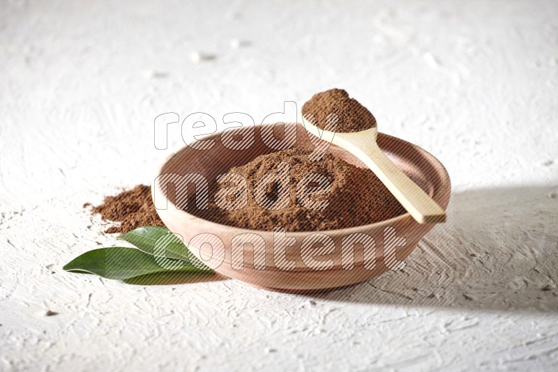 A wooden bowl and a wooden spoon full of cloves powder on a textured white flooring