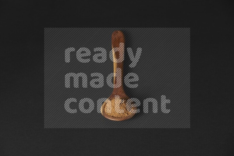 Cinnamon powder in a spoon ladle on black background