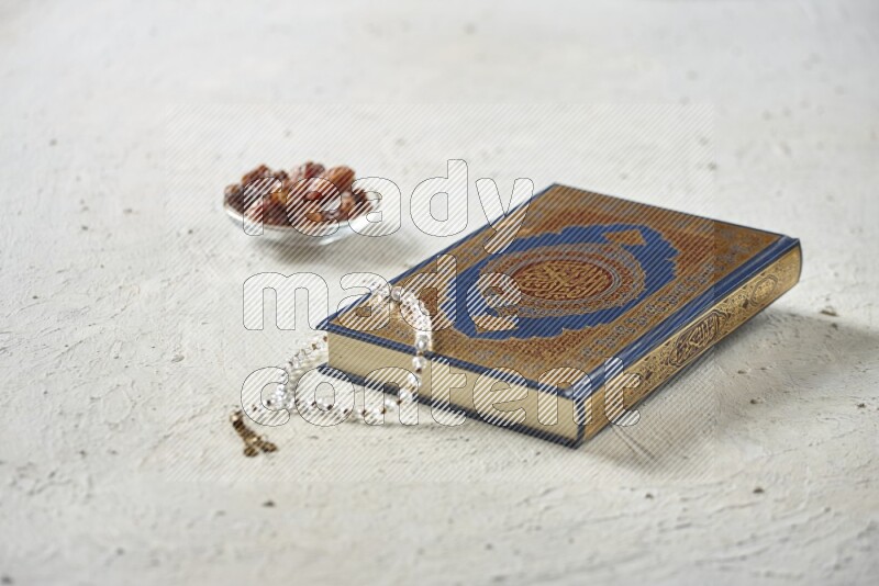 Quran with dates, prayer beads and different drinks all placed on textured white background