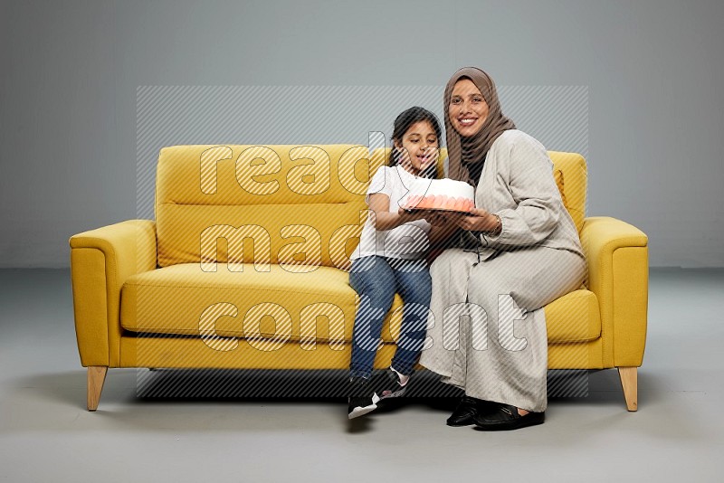 A girl sitting giving a cake to her mother on gray background