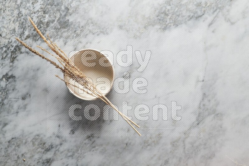 Wheat stalks on beige pottery bowl on grey marble background
