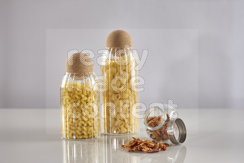 Raw pasta in glass jars with chilis on light grey background