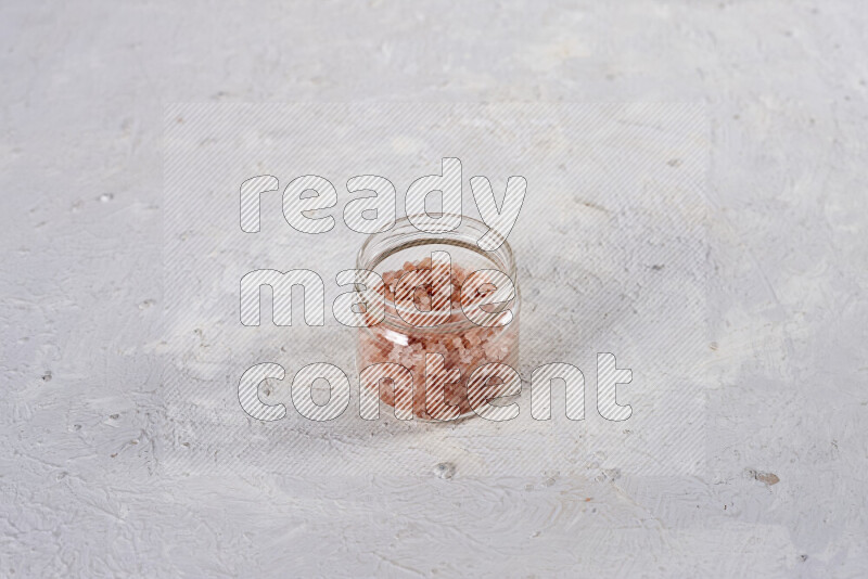 A glass jar full of coarse himalayan salt crystals on white background