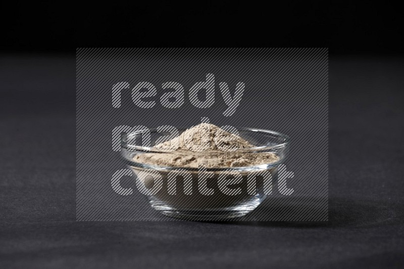 A glass bowl full of garlic powder on a black flooring