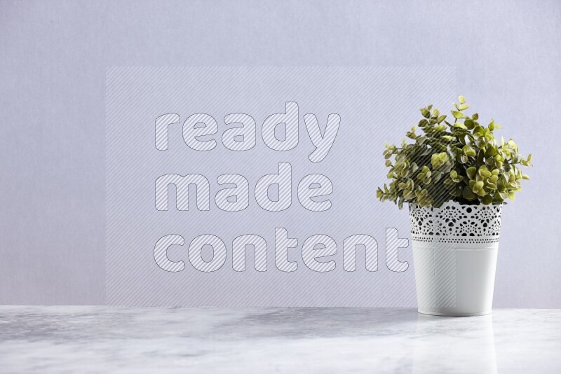 Green artificial plant in white decorative pot on grey marble background