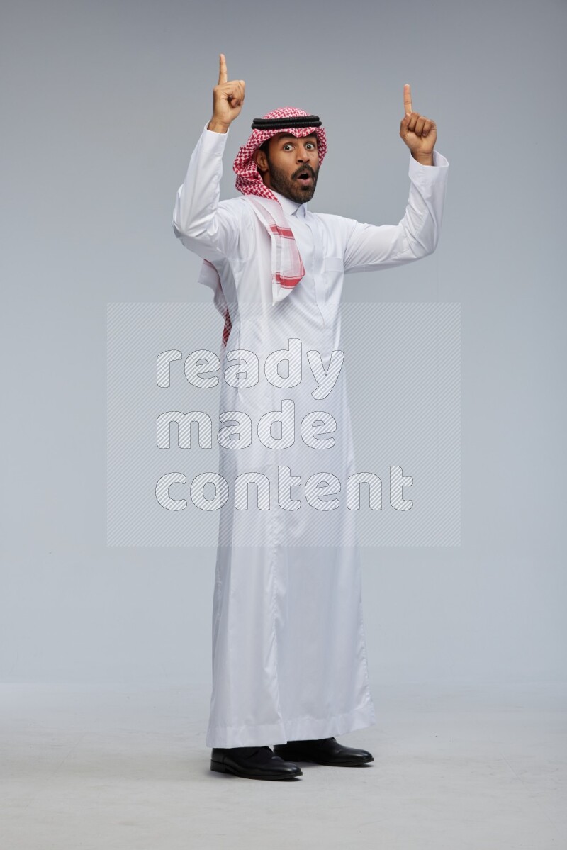 Saudi man Wearing Thob and shomag standing interacting with the camera on Gray background