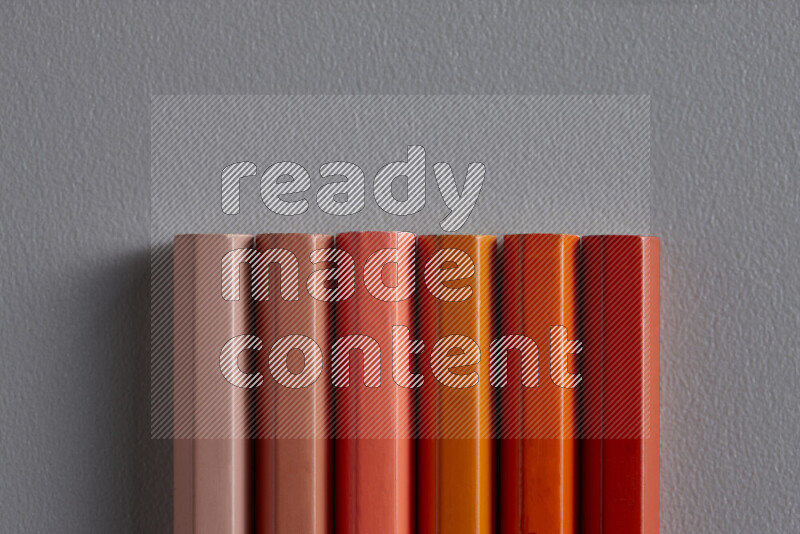 A collection of colored pencils arranged showcasing a gradient of orange hues on grey background