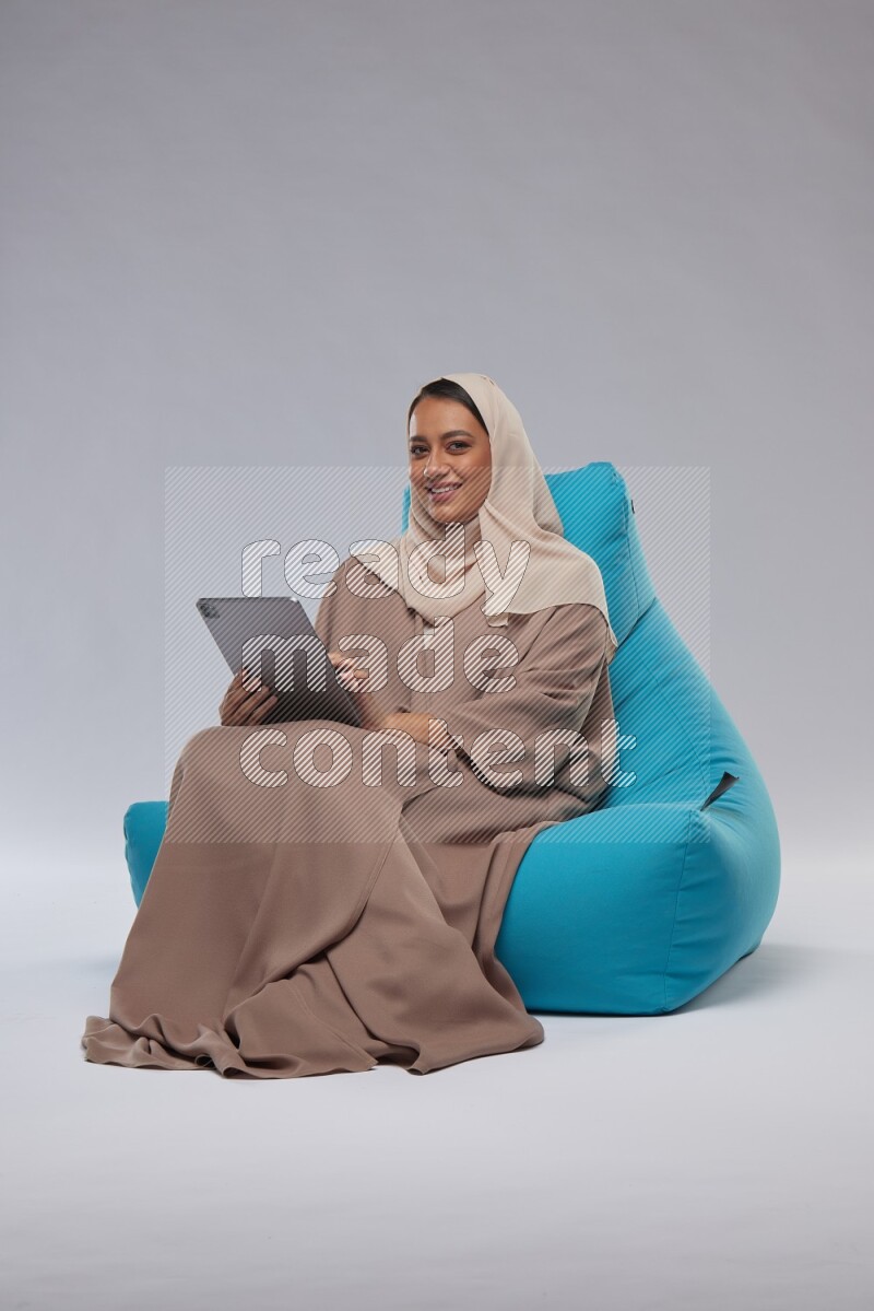 A Saudi woman sitting on a blue beanbag and working on tablet
