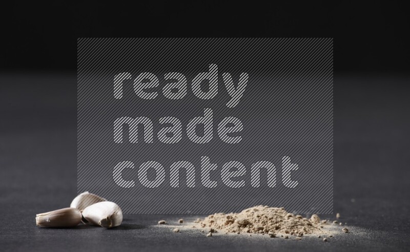 A small pile of garlic powder with some of cloves and a whole garlic bulb on a black flooring