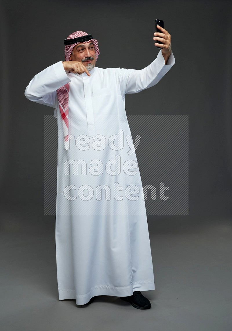 Saudi man with shomag Standing taking selfie on gray background