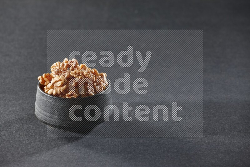 A black pottery bowl full of peeled walnuts on a black background in different angles