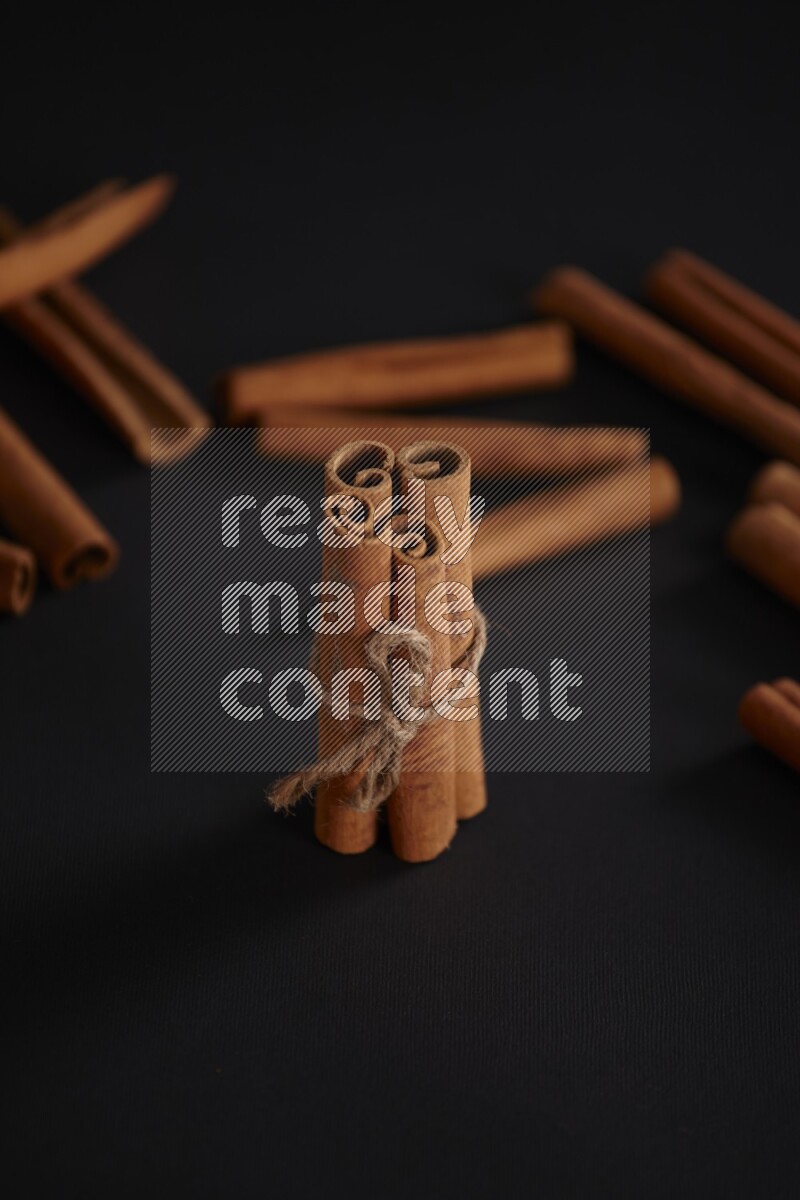 4 Cinnamon sticks stacked and bounded with more sticks in the background on black flooring