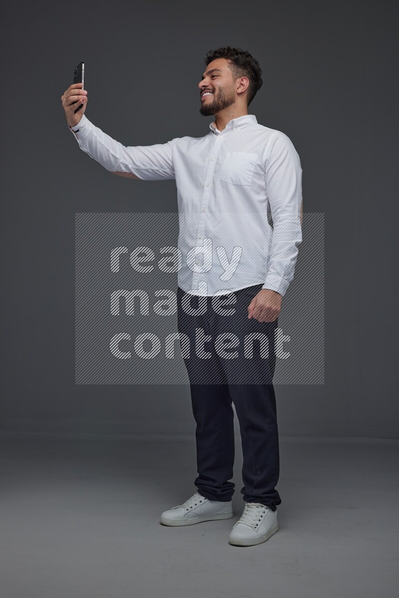 A man wearing smart casual and taking selfie with his phone eye level on a gray background