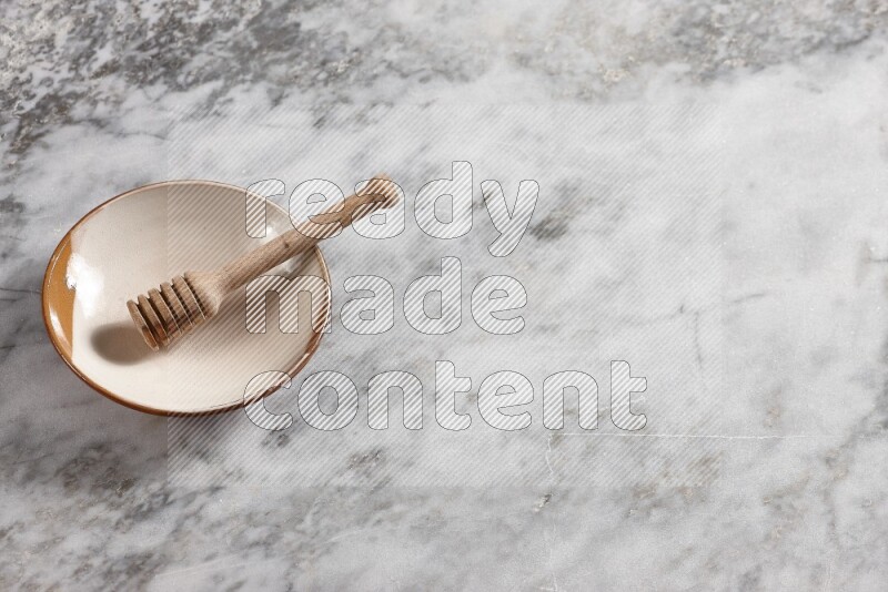 Multicolored pottery plate with wooden honey dipper in it on grey marble background
