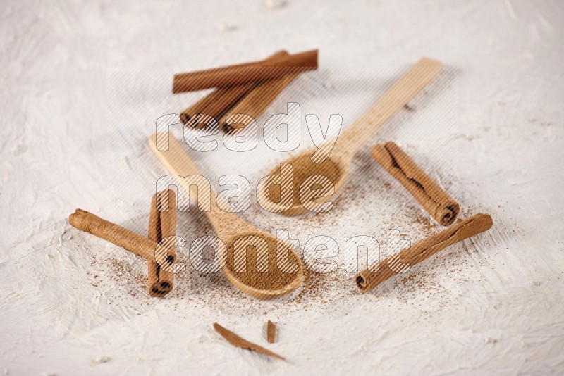 Two wooden spoons full of cinnamon powder with cinnamon sticks on white background