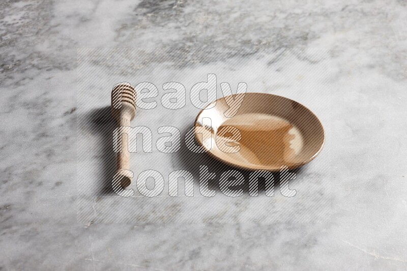 Multicolored pottery plate with wooden honey dipper on the side on grey marble background