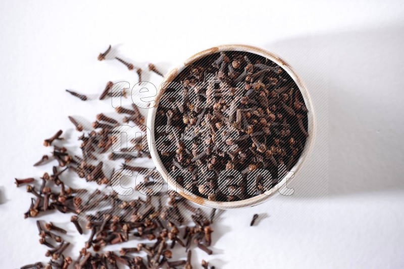 A beige ceramic bowl full of cloves on a white flooring