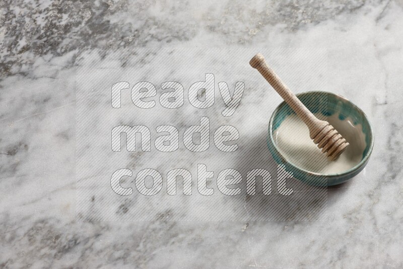 Multicolored pottery bowl with wooden honey dipper in it on grey marble background
