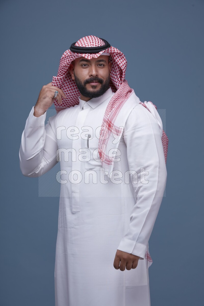 A Saudi man posing on blue background wearing Thob and Shomag
