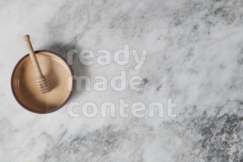 طبق فرن فخاري بيج مع ملعقة عسل خشبية بداخله على خلفية من الرخام الرمادي