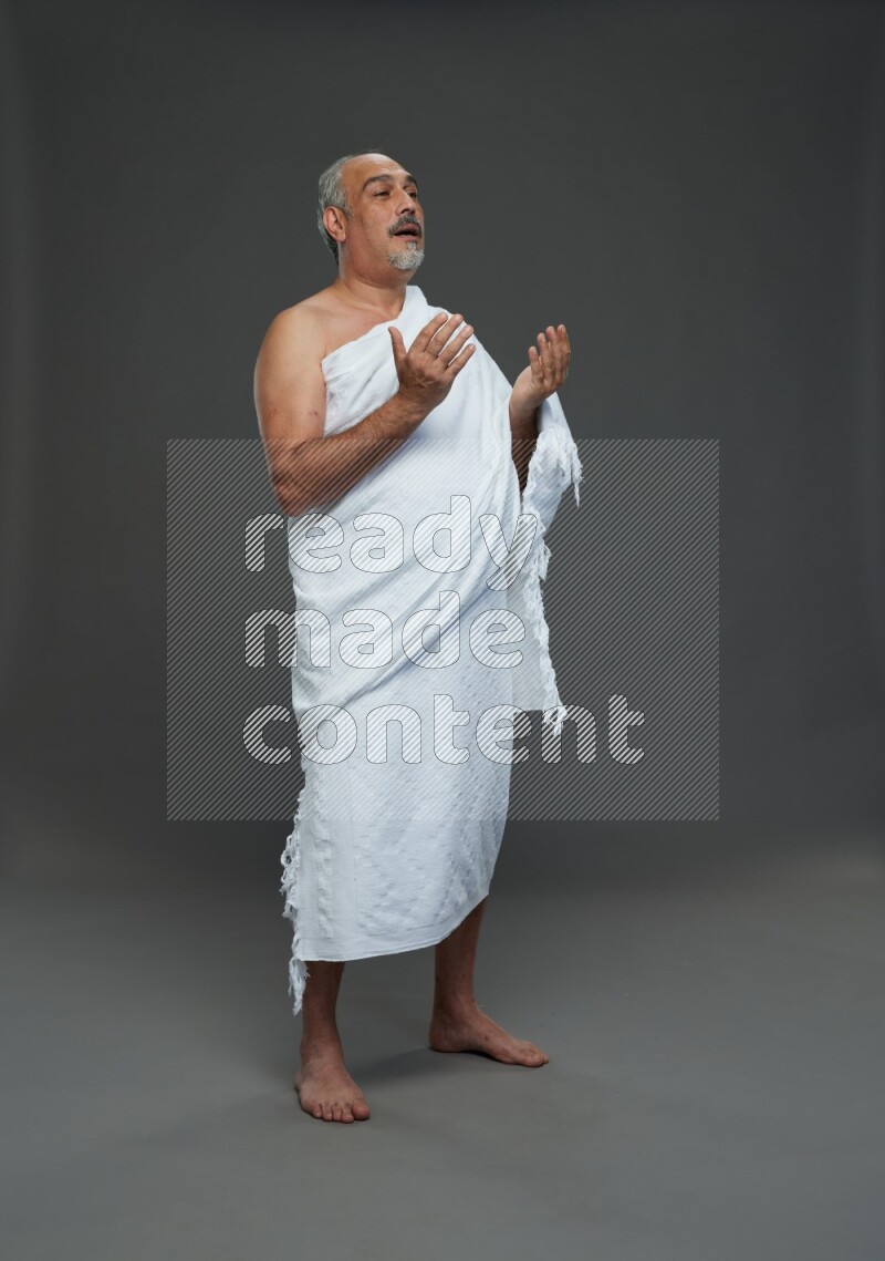 A man wearing Ehram Standing dua'a on gray background