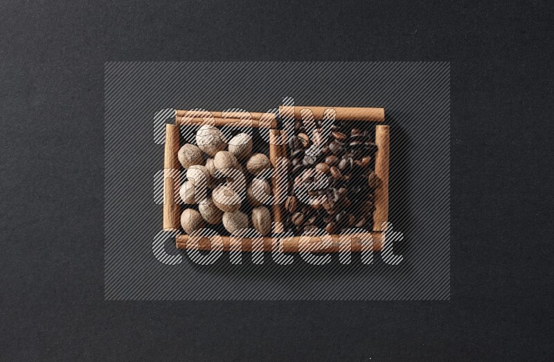 مربعان من أعواد القرفة ممتلئان بحبوب القهوة وجوزة الطيب علي خلفية سوداء