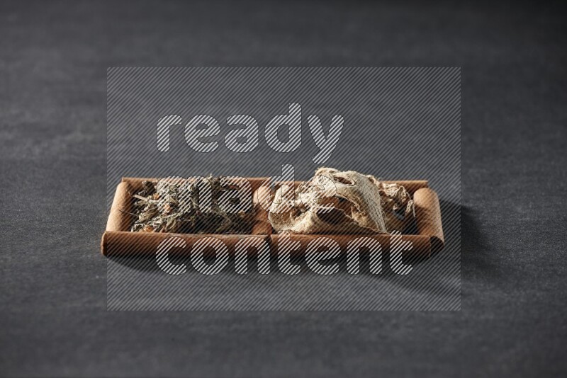 مربعان من أعواد القرفة ممتلئان بالزنجبيل المجفف والريحان المجفف علي خلفية سوداء