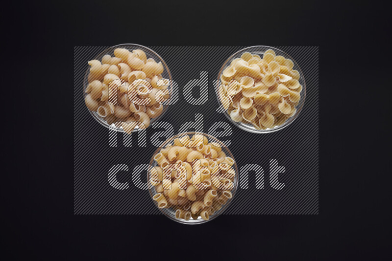 Different pasta types in glass bowls on black background