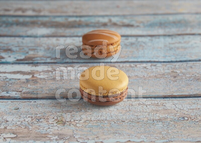 45º Shot of of two assorted Brown Irish Cream, and Yellow, and Brown Chai Latte macarons  on light blue background