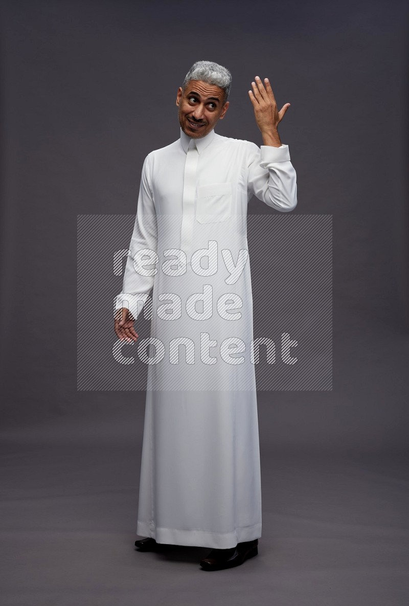 Saudi man wearing thob standing interacting with the camera on gray background