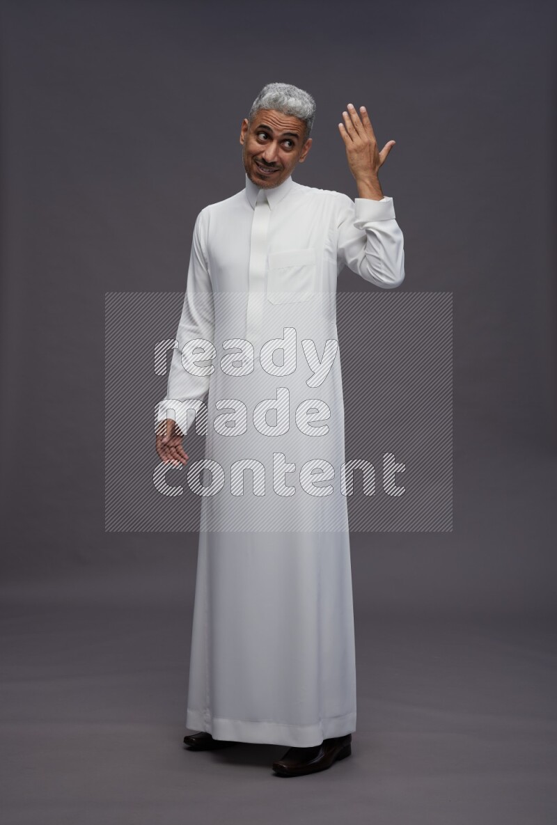 Saudi man wearing thob standing interacting with the camera on gray background