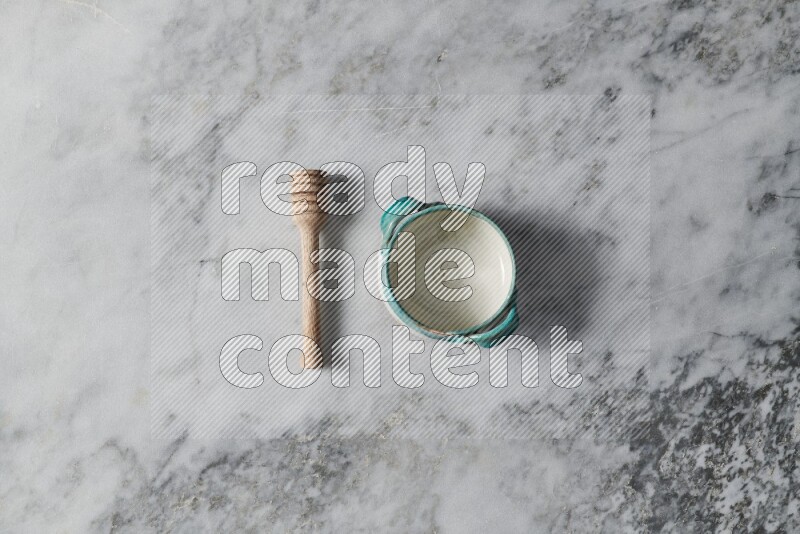 Multicolored pottery bowl with wooden honey dipper on the side on grey marble background