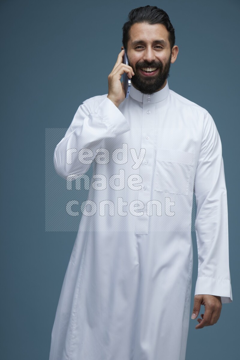 A man having a call on a blue background wearing Saudi Thob