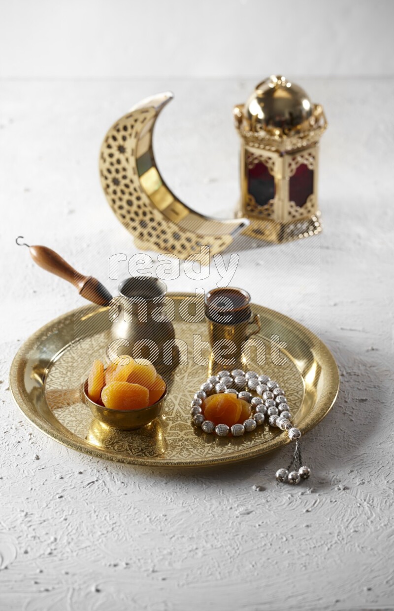 مشمش مجفف في وعاء معدني مع قهوة وسبحة على صينية بجانب فوانيس علي خلفية بيضاء