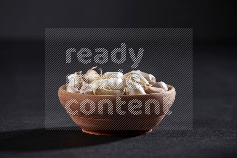 A wooden bowl full of garlic cloves on a black flooring in different angles