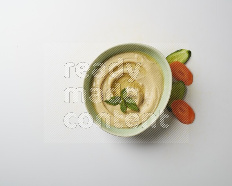 Hummus in a green plate garnished with mint on a white background