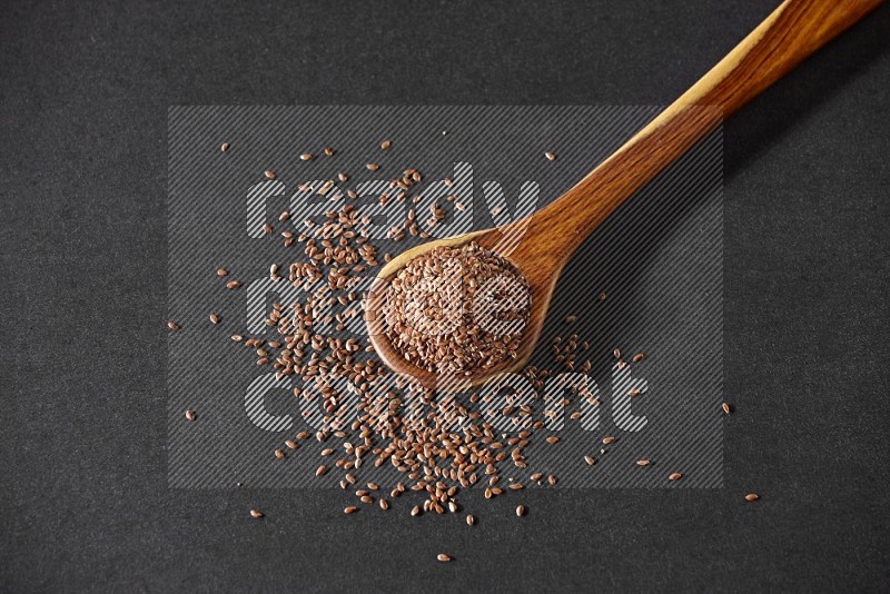 A wooden ladle full of flax and seeds spreaded beside it on a black flooring in different angles