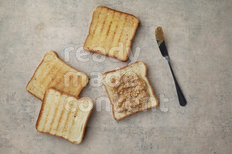 Crunchy peanut butter on a toasted white toast and toasted white toast slices on a light blue textured background