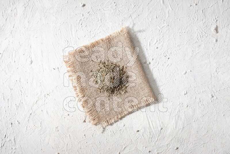 Cumin seeds on a burlap piece on a textured white flooring