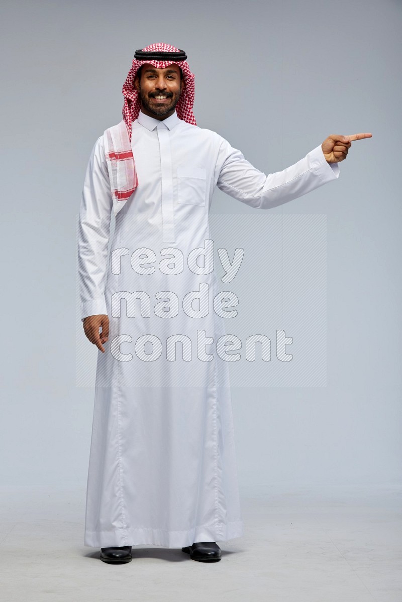 Saudi man Wearing Thob and shomag standing interacting with the camera on Gray background