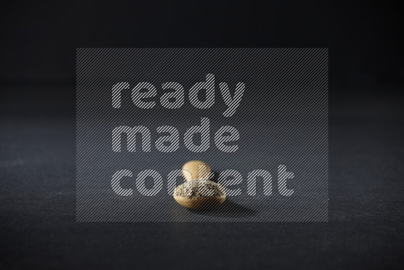 A wooden spoon full of cardamom powder on black flooring